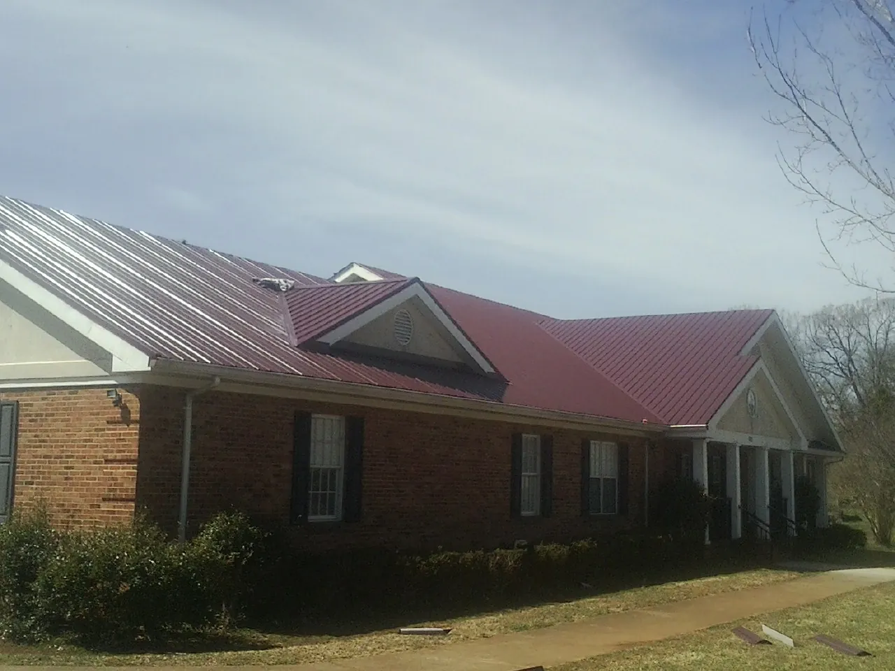 Red metal roof with gabled entries on a long brick building, from a Hail Damage Roof Repair job in Crane Hill