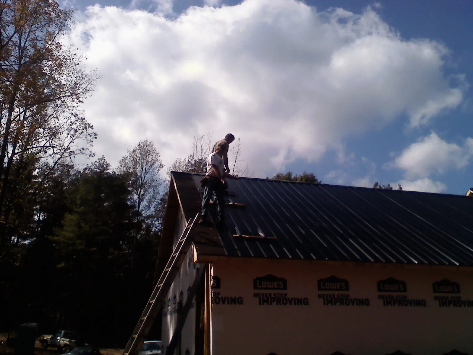 Roofer fastening dark metal panels high against a cloudy sky, from a Roof Inspection job in Crane Hill