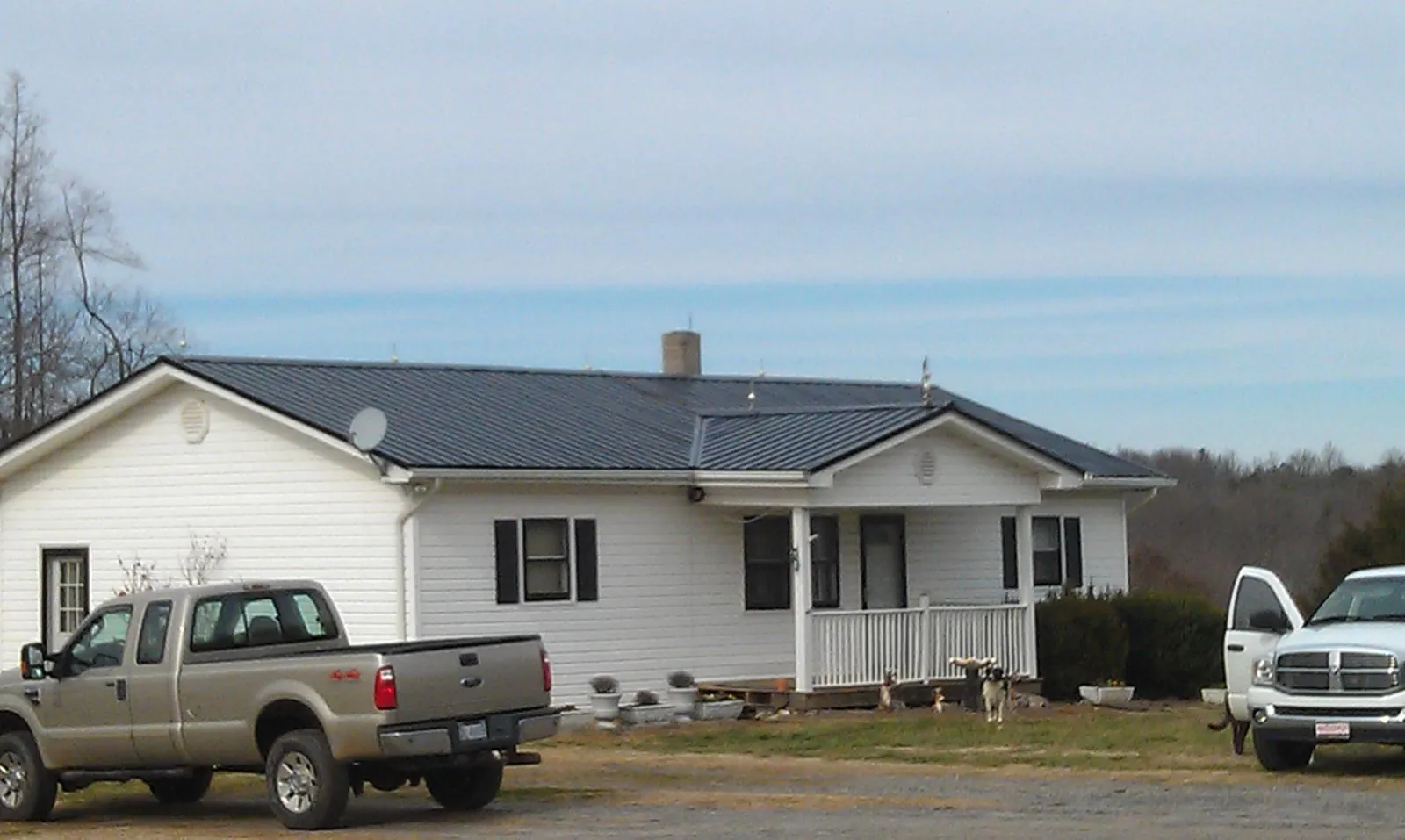 Finished dark metal roof on a white ranch home with work trucks parked in Crane Hill