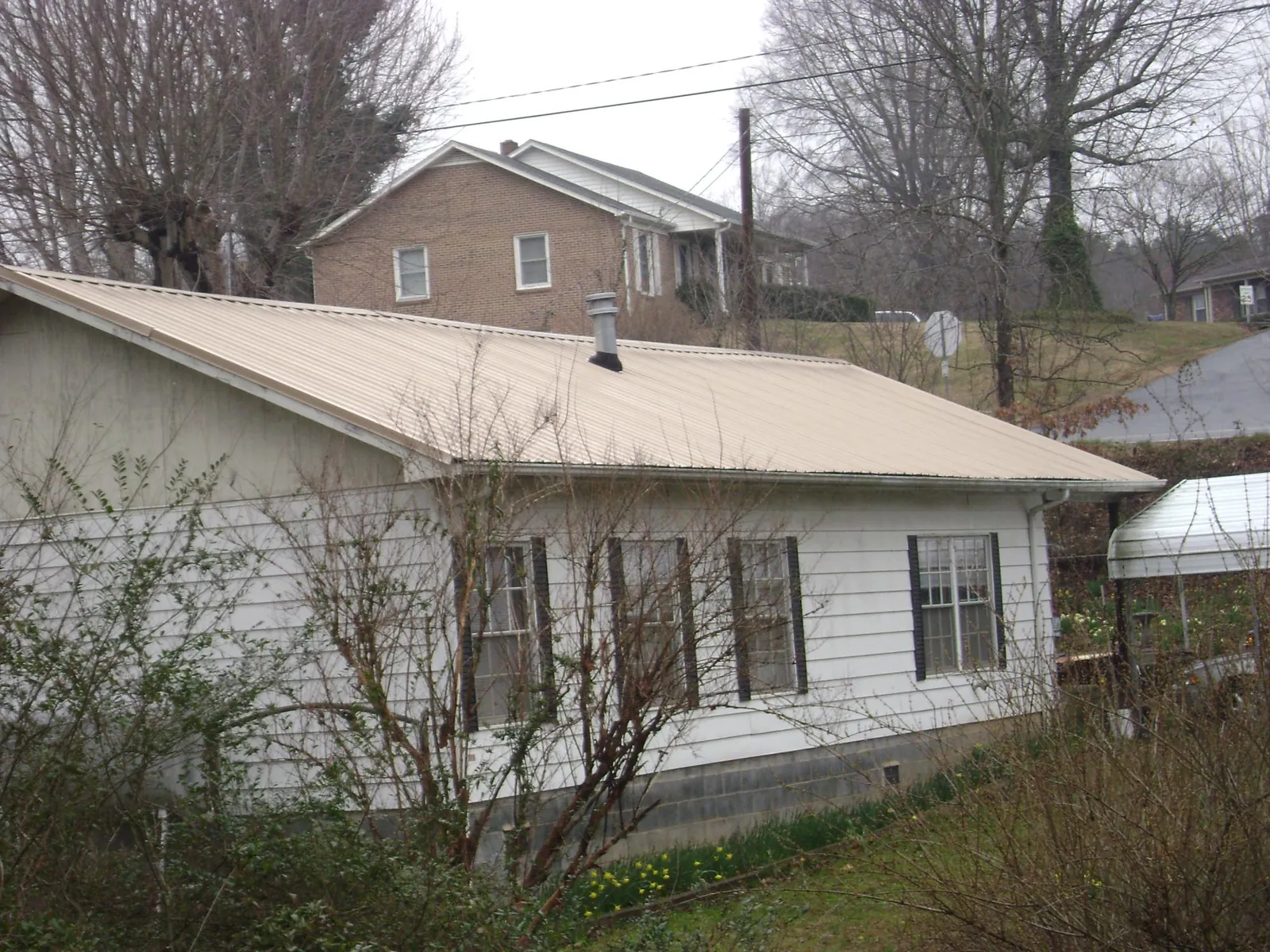 Tan metal roof on a white sided house set into a hillside — Commercial Roofing by Roofing Brothers in Crane Hill
