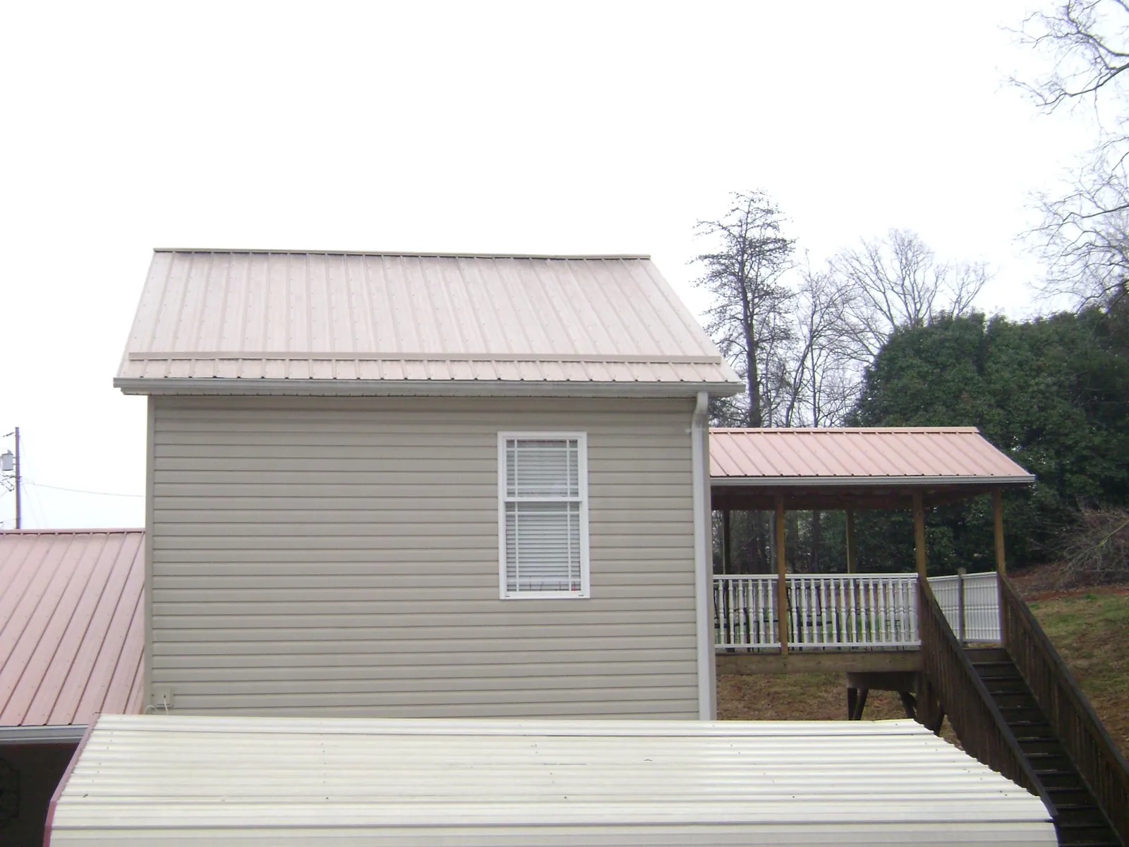 Tan metal roofs on a two story addition and attached porch, from a Roof Replacement job in Crane Hill